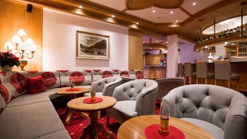 Eine gemütliche Lounge mit grauen Sofas und einem runden Tisch. Im Hintergrund ist eine Bar und eine dekorative Beleuchtung zu sehen.