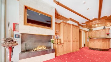 Ein gemütliches Wohnzimmer mit einem modernen Kamin und einem Fernseher. Der Raum ist mit Holzdetails und einem roten Teppich ausgestattet.