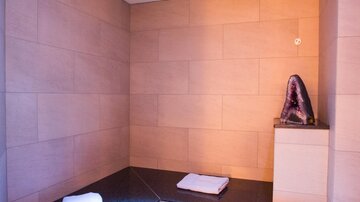 Ein entspannender Innenraum mit einer Sauna. Auf dem Stein sitzt ein großer Amethyst und es liegen zwei Handtücher bereit.
