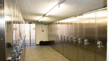 Ein schmaler Flur mit metallenen Schließfächern auf beiden Seiten. Am Ende des Flurs befindet sich eine Tür, die nach außen führt.