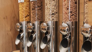 Eine moderne Müsli-Bar mit verschiedenen Getreidearten in transparenten Spendern. Die Spender sind aus Edelstahl und bieten eine praktische Möglichkeit, Müsli abzufüllen.