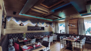 Ein gemütliches Restaurant mit Holzelementen und stilvollen Möbeln. Die Wände sind mit einer kunstvollen Berglandschaft dekoriert.