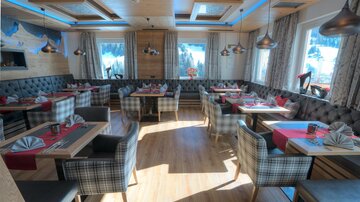 Ein gemütliches Restaurant mit Holzmöbeln und schön dekorierten Tischen. Große Fenster bieten einen Blick auf die Landschaft.