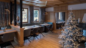 Ein stilvolles Restaurant mit Holzelementen und modernen Möbeln. Ein geschmückter Weihnachtsbaum verleiht dem Raum eine festliche Atmosphäre.