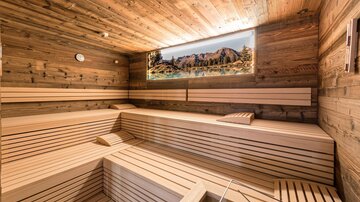 Eine moderne Sauna aus hellem Holz mit mehreren Bankreihen. Ein Bild einer Berglandschaft dekoriert die Wand und schafft eine entspannende Atmosphäre.