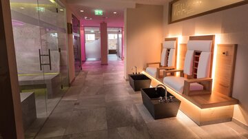 Ein eleganter Spa-Bereich mit hellen Wänden und stilvollen Sitzgelegenheiten. Im Hintergrund sind entspannende Fußbäder sichtbar.