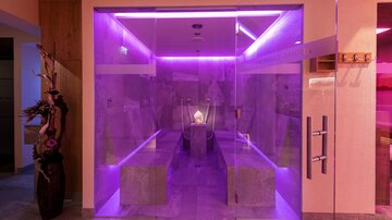 Ein modernes Spa mit einem gläsernen Eingang und stimmungsvollem, lila Licht. Der Innenraum wirkt entspannend und einladend.