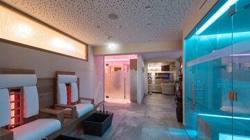 Ein moderne Wellnessbereich mit bequemen Liegen und farbigem Licht. Der Raum wirkt entspannend und einladend.
