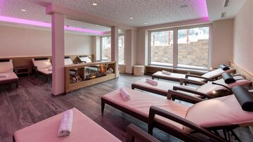 Ein gemütlicher Wellnessbereich mit Liegen und sanfter Beleuchtung. Große Fenster bieten einen Blick auf die Natur.
