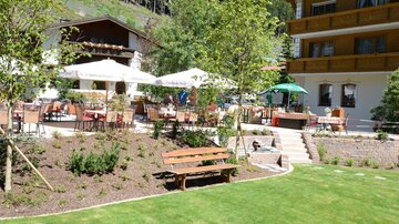 Ein schöner Garten mit Sitzmöglichkeiten und Sonnenschirmen. Im Hintergrund ist ein Gebäude zu sehen, das die Atmosphäre entspannend macht.