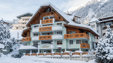 Ein charmantes Hotel im Schnee mit Holzbalkonen. Umgeben von verschneiten Bergen und einer malerischen Winterlandschaft.