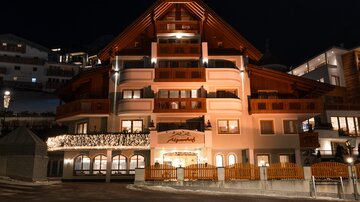 Ein schön beleuchtetes Hotelgebäude in einer Berglandschaft bei Nacht. Die Architektur verbindet traditionellen und modernen Stil.