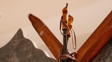 Zwei Holzski sind gekreuzt und mit einem Skibindungssystem versehen. Im Hintergrund ist eine graue Wand zu sehen.