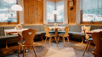 Ein gemütliches Restaurant mit Holzverkleidung und liebevoll dekorierten Tischen. Die Sitzgelegenheiten bestehen aus Bänken und Holzstühlen, die eine einladende Atmosphäre schaffen.