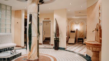 Ein eleganter Wellnessbereich mit einem runden Mosaikboden und modernen Einrichtungen. Die entspannende Atmosphäre wird durch sanfte Beleuchtung und dekorative Pflanzen verstärkt.