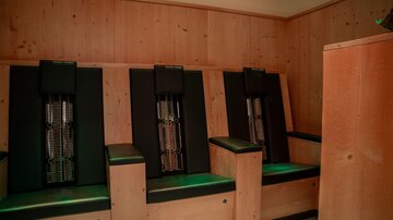 Ein entspannender Raum mit modernen, schwarzen Liegen. Die Wände sind aus hellem Holz, was eine gemütliche Atmosphäre schafft.