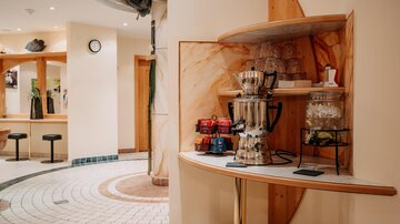 Ein moderner Eingangsbereich mit einem dekorativen Regal. Auf dem Regal steht eine Kaffeemaschine und Geschirr, während der Boden mit eleganten Fliesen gestaltet ist.