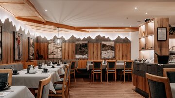 Ein gemütliches Restaurant mit Holzverkleidung und eleganten Tischen. Wände mit malerischen Fotografien schaffen eine einladende Atmosphäre.
