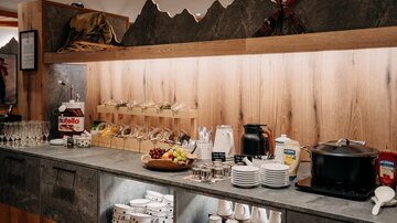 Ein gut sortiertes Buffet mit verschiedenen Speisen und Getränken. Holzregale und eine gemütliche Atmosphäre schaffen eine einladende Umgebung.