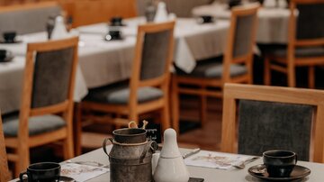 Ein gemütliches Restaurant mit Holzmöbeln und gedeckten Tischen. Auf den Tischen stehen Kaffeetassen und Servietten.