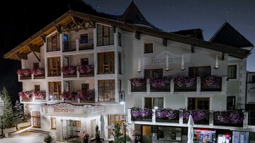 A beautiful hotel with blooming balcony plants and an inviting entrance area. The surroundings are quiet and the night has a clear starry sky.