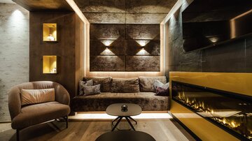 A modern living room with an elegant sofa and a warm fireplace. The walls are designed with stylish accents and lighting.