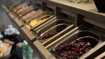 A buffet with various foods, including dried fruits and nuts. In the background, there are fresh apples and yogurt cups.