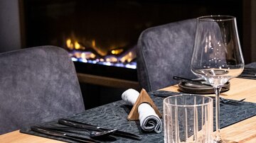 An elegant restaurant with a beautifully set table. In the background, a cozy fireplace can be seen.