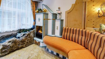 Ein gemütlicher Raum mit einem orangenen Sofa und einem eleganten Kamin. Große Fenster sorgen für viel Tageslicht und eine angenehme Atmosphäre.