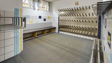 Ein funktionaler Raum mit Bänken und Wandhaken. Helle Fliesen und Fenster sorgen für eine angenehme Atmosphäre.