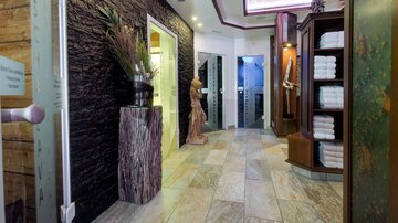 Ein moderner Wellnessbereich mit Steinwänden und eleganten Details. Im Hintergrund sind Türen zu verschiedenen Behandlungsräumen sichtbar.
