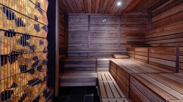 Ein gemütlicher Saunaraum mit Holzverkleidung und Sitzbänken. An der Wand sind stapelbare Holzscheite sichtbar.