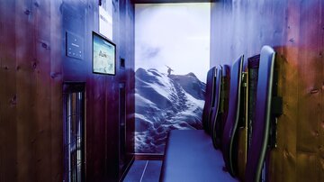 Ein moderner Entspannungsraum mit Holzverkleidung und bequemen Sitzgelegenheiten. An der Wand ist ein Bild einer schneebedeckten Berglandschaft.