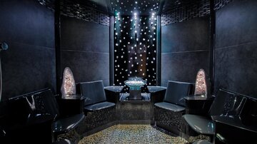 Ein eleganter Raum mit schwarzem Interieur und bequemen Sitzen. Die Decke ist mit funkelnden Lichtern geschmückt, die eine entspannte Atmosphäre schaffen.