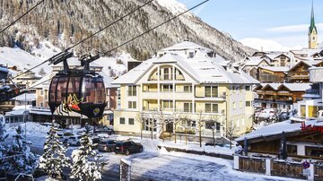 Eine malerische Winterlandschaft mit schneebedeckten Bergen und einem Seilbahnzug. Im Vordergrund ist ein charmantes Gebäude sichtbar.