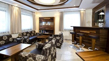 Ein stilvolles Wohnzimmer mit modernen Möbeln und einer gemütlichen Bar. Große Fenster lassen viel Licht hinein und sorgen für eine einladende Atmosphäre.