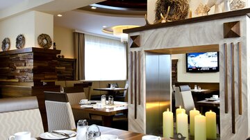 Ein modernes Restaurant mit elegantem Interieur und Tischen, die für Gäste gedeckt sind. Im Hintergrund sind Kerzen und ein Fernseher zu sehen.