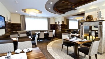 Ein modernes Restaurant mit eleganten Möbeln und gut gedeckten Tischen. Große Fenster sorgen für viel Tageslicht und eine angenehme Atmosphäre.