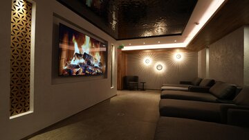 Ein ruhiger Entspannungsraum mit gemütlichen Liegen. An der Wand befindet sich ein großer Bildschirm mit einem digitalen Kaminfeuer.