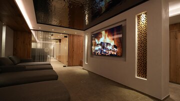 Ein eleganter Entspannungsraum mit bequemen Liegen und einer großen Wand mit einem digitalen Kamin. Die Atmosphäre ist ruhig und modern mit warmen Holztönen.