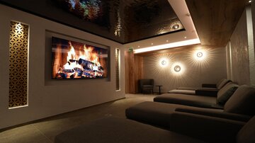 Ein moderner Entspannungsraum mit gemütlichen Liegen. An der Wand befindet sich ein großes Bild mit einem lodernden Feuer.