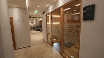 Ein moderner, heller Spa-Bereich mit Holzdetails und sanfter Beleuchtung. Der Flur führt zu einer Sauna mit einer dekorativen Glaswand.