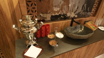 Ein eleganter Samowar steht auf einer Holzoberfläche. Daneben befinden sich eine Schale mit Süßigkeiten und ein dekoratives Waschbecken.