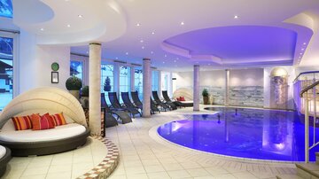 An elegant wellness area with a blue pool and comfortable loungers. The atmosphere is relaxing with soft lighting and modern design elements.