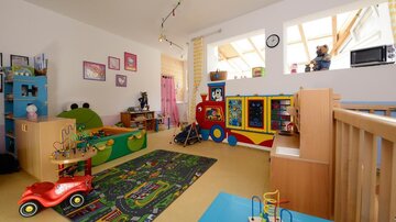A colorful children's room with toys, a carpet, and a play area. There is a play corner with a toy bus and a red car.