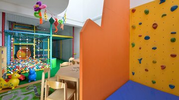 A colorful playground for children with a ball pit and a climbing wall. There are also play tables and colorful wall surfaces.