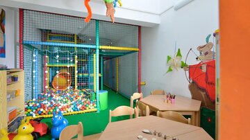 A bright playroom with a colorful ball pit and a play tower. Around the tables are colorful toys and art supplies.