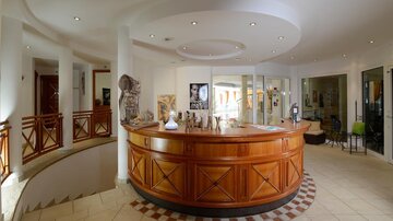 A bright reception area with a round wooden reception desk. The walls are decorated with artworks and decorations.