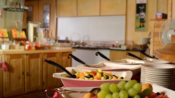A colorful buffet with fresh fruit in bowls. In the background, a cozy hospitality environment can be seen.