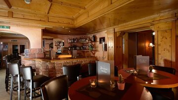 A cozy bar with wood paneling and an inviting atmosphere. The tables are set and the bar is well stocked.